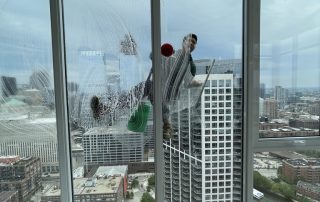 Professional high-rise window cleaner working on a luxury Chicago apartment building with city skyline view.