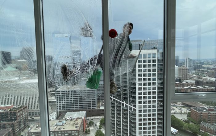 Professional high-rise window cleaner working on a luxury Chicago apartment building with city skyline view.