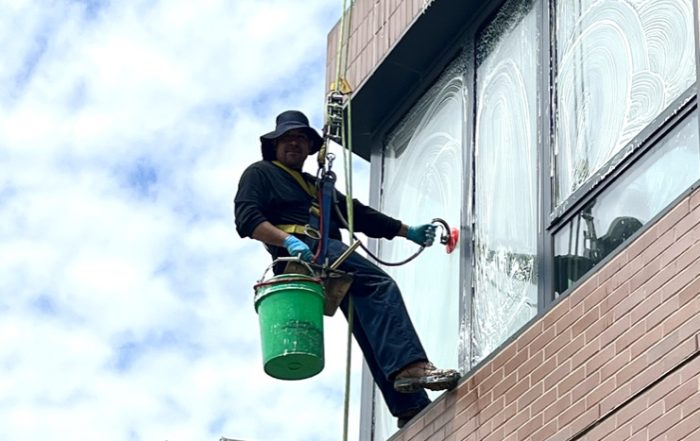 Professional technician conducting commercial window washing on a Midwest high-rise building with fall protection equipment