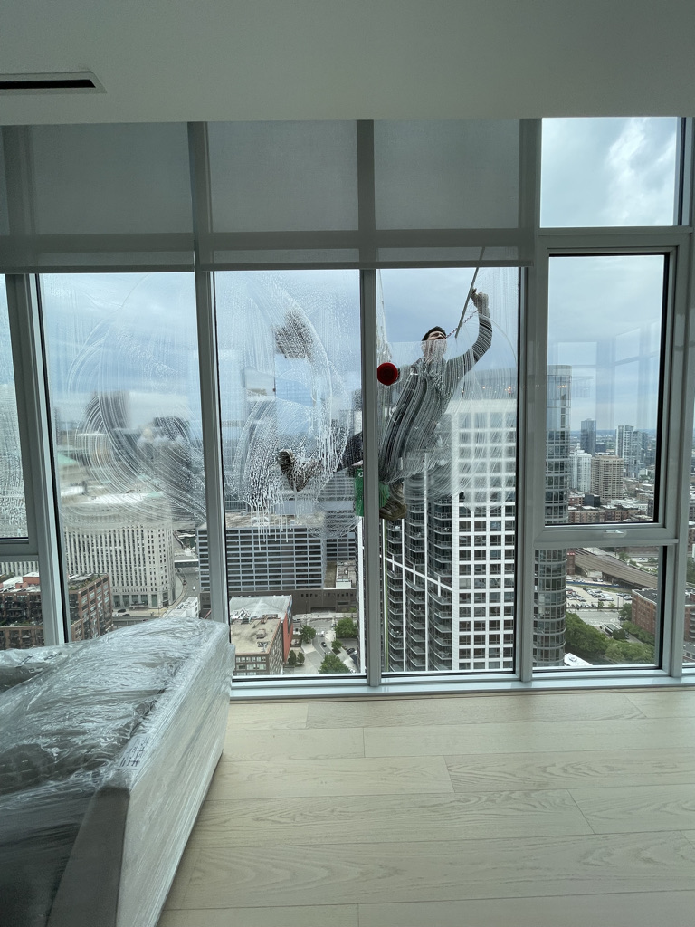 Window washer cleaning exterior high-rise apartment windows with a squeegee