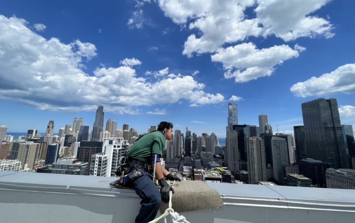 Technician performing exterior maintenance services on a Kansas City high-rise under clear blue sky
