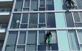 2 window washers cleaning exterior windows of a high rise luxury apartment building