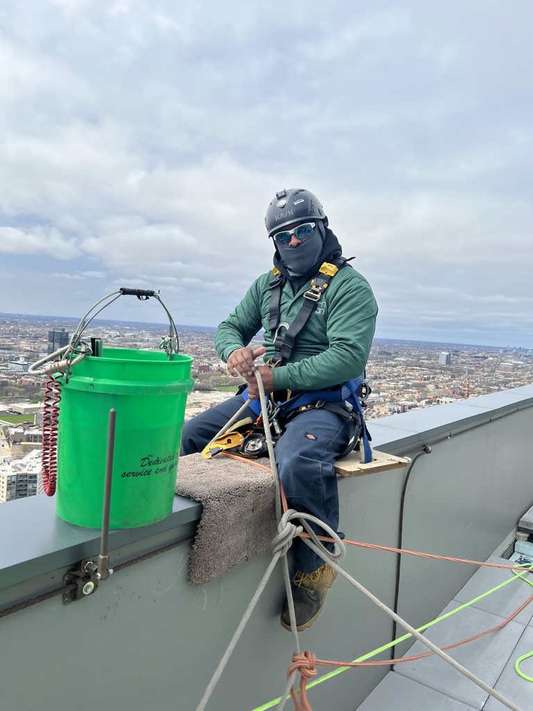 Window washer checking harness & safety gear before cleaning high rise windows