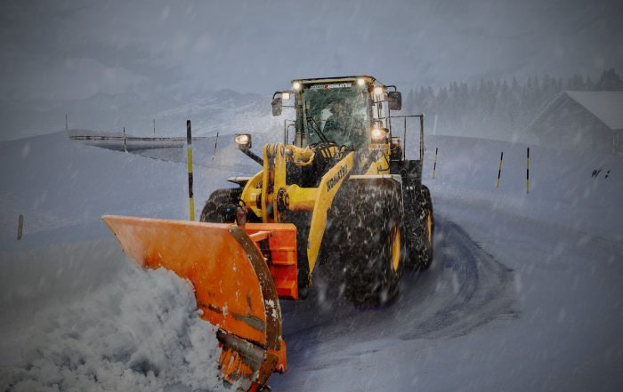A snow plow truck clearing heavy snow on a Minneapolis roadway during winter, showcasing professional snow removal services by Ascent Building Service.